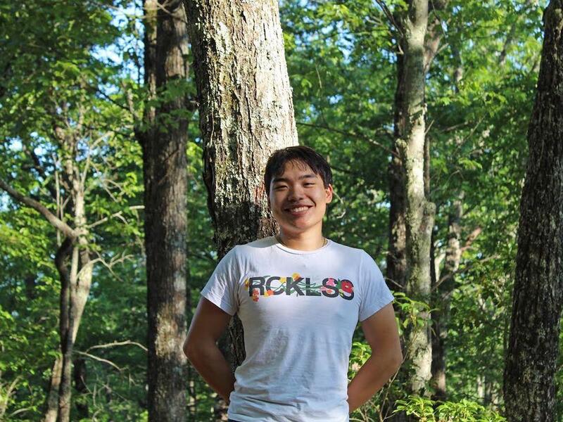 Man stands in front of a tree in a T-shirt and smiles.