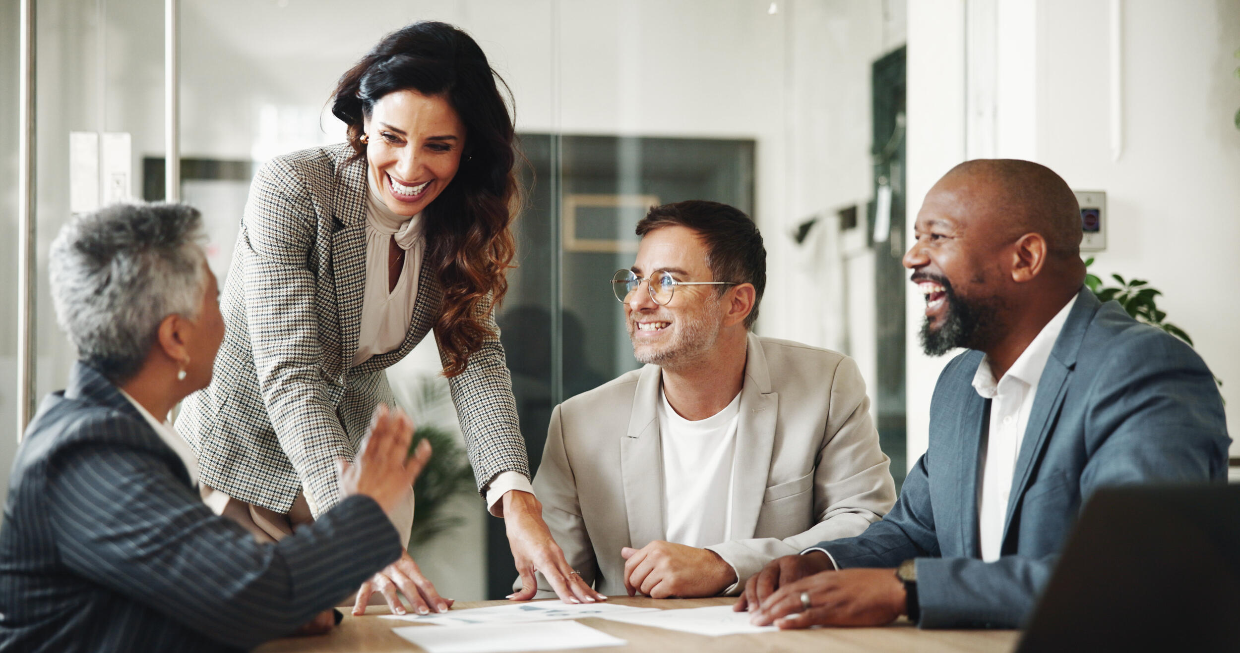 A photo of a woman standing at a table where a woman and two men are sitting. They are all smiling. 
