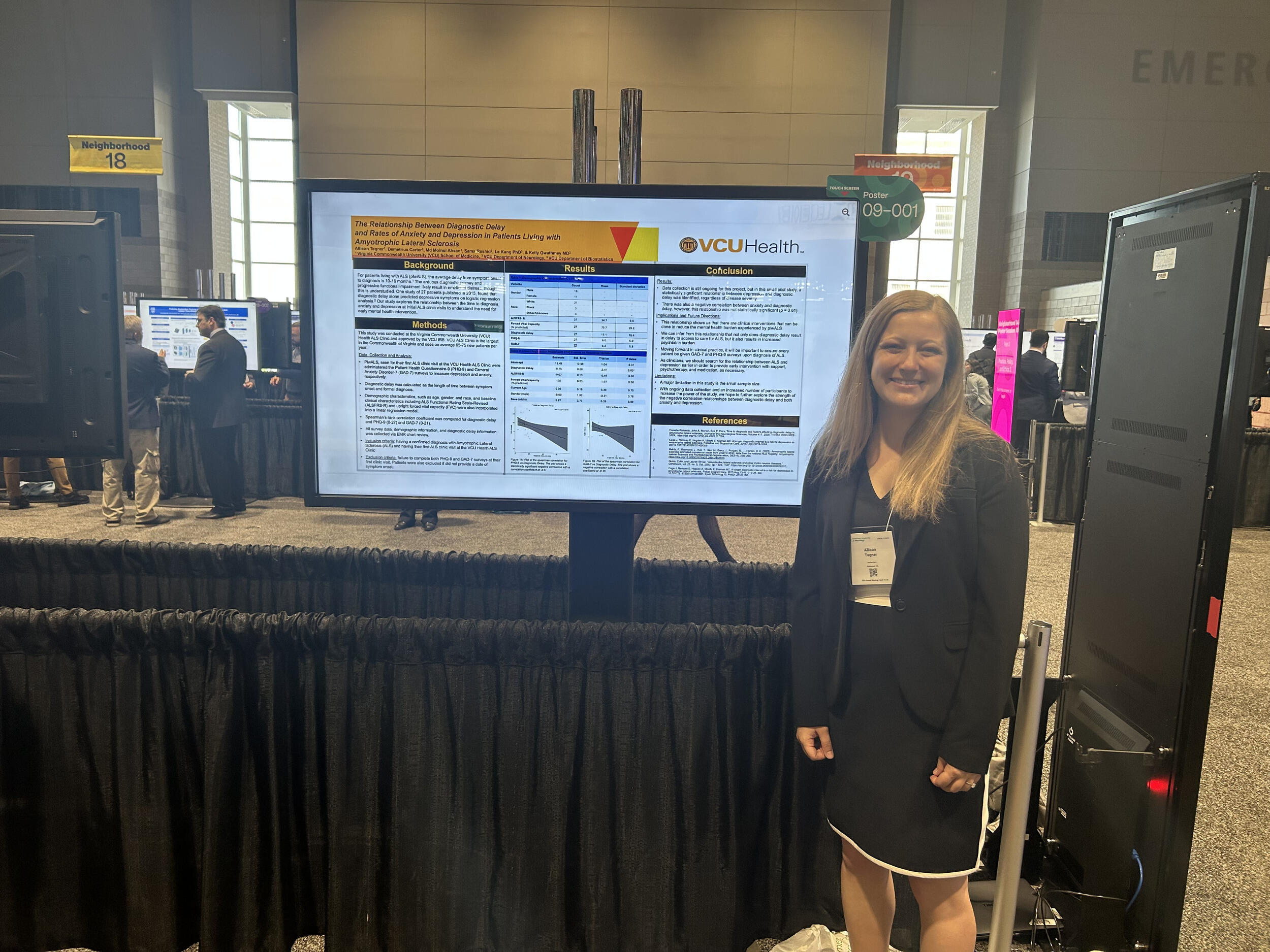 A photo of a woman standing next to a screen displaying her research. 