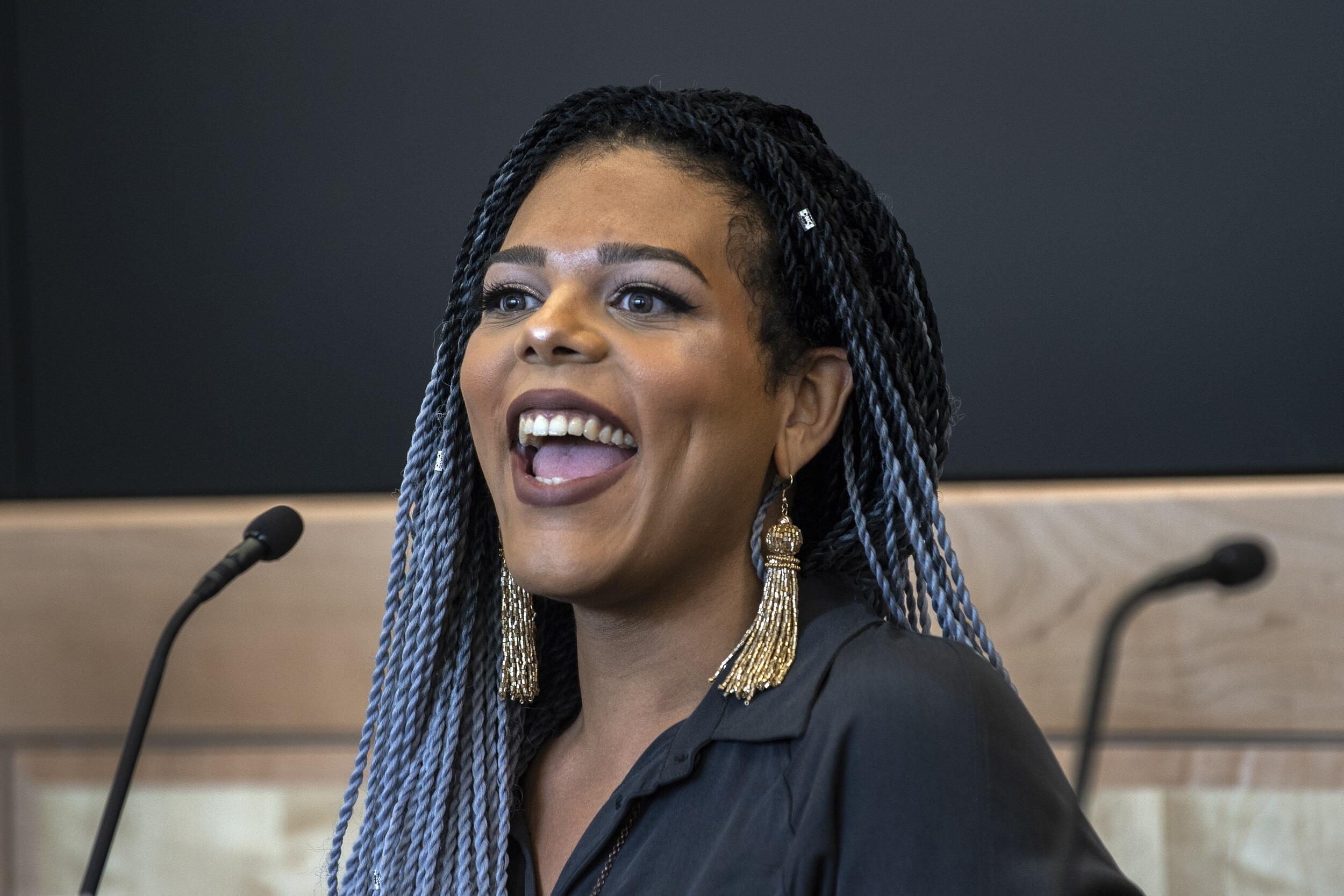 Austyn Higgs speaking at a podium during the symposium.