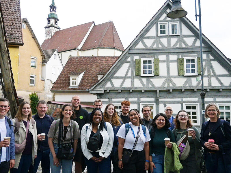 A group photo of 15 people standing in front of historic German buildings. 