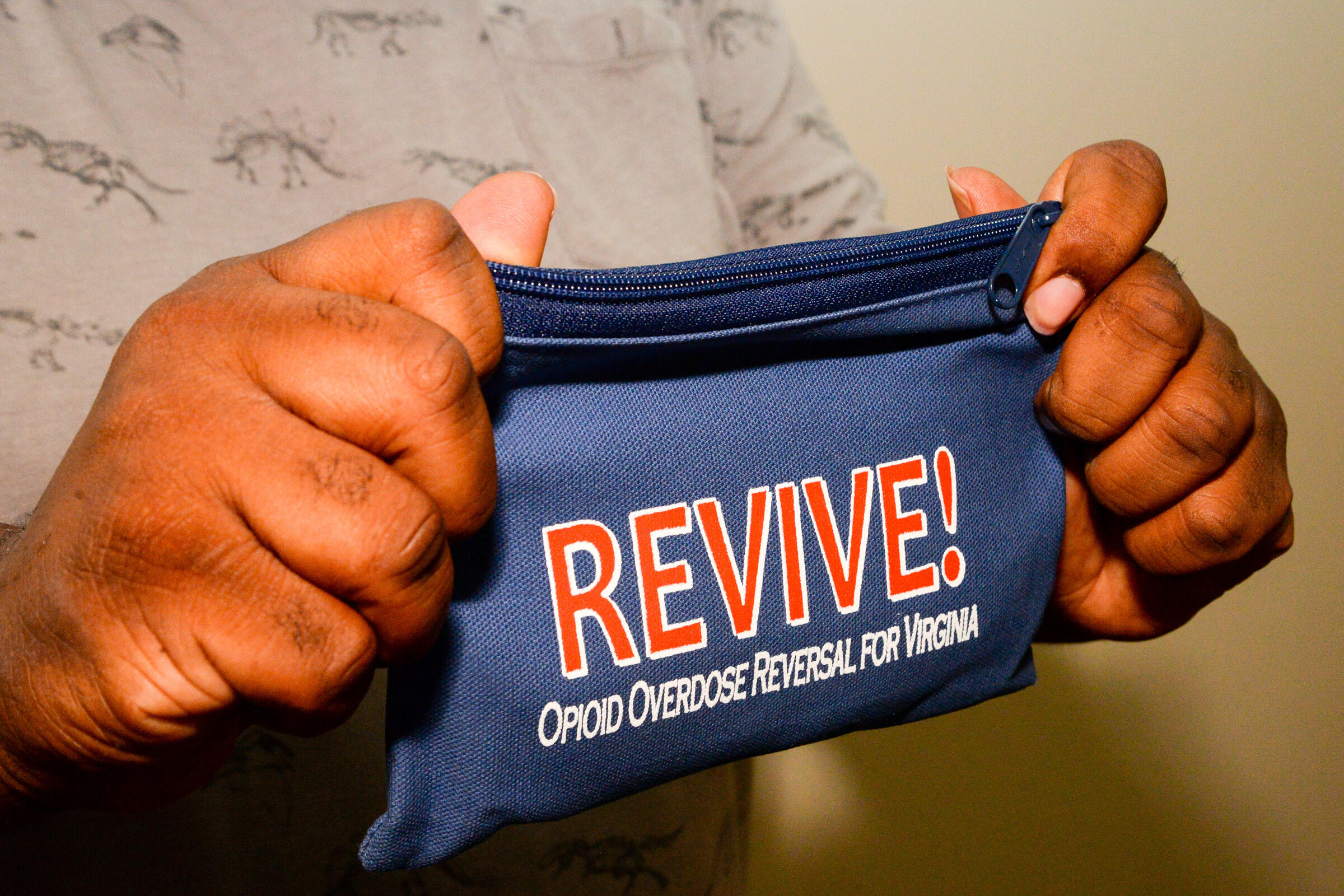 A man holds a small blue zipper bag labelled REVIVE - opioid overdose reversal for Virginia