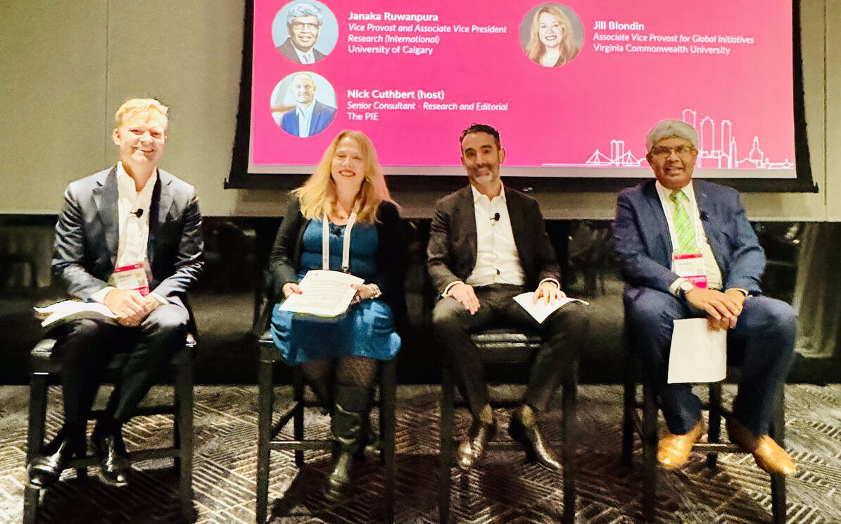A photo of four people sitting in chairs in front of a projector screen. 
