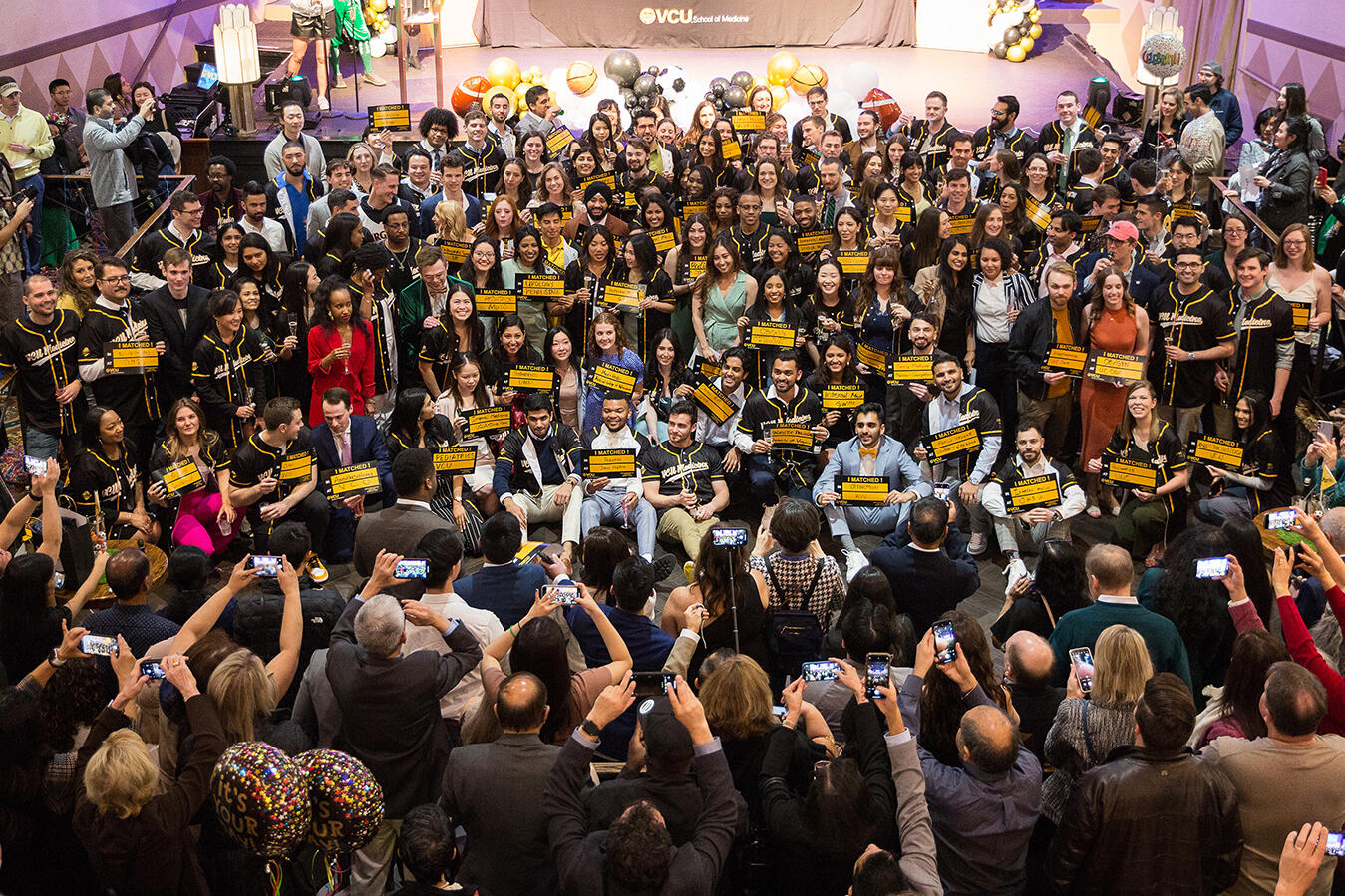 A large crowd of people standing in a circle, some of them are holding up yellow signs with black text