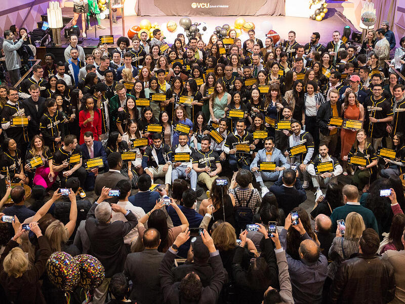 A large crowd of people standing in a circle, some of them are holding up yellow signs with black text