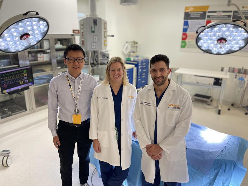 A photo of three people standing in a surgery room. 
