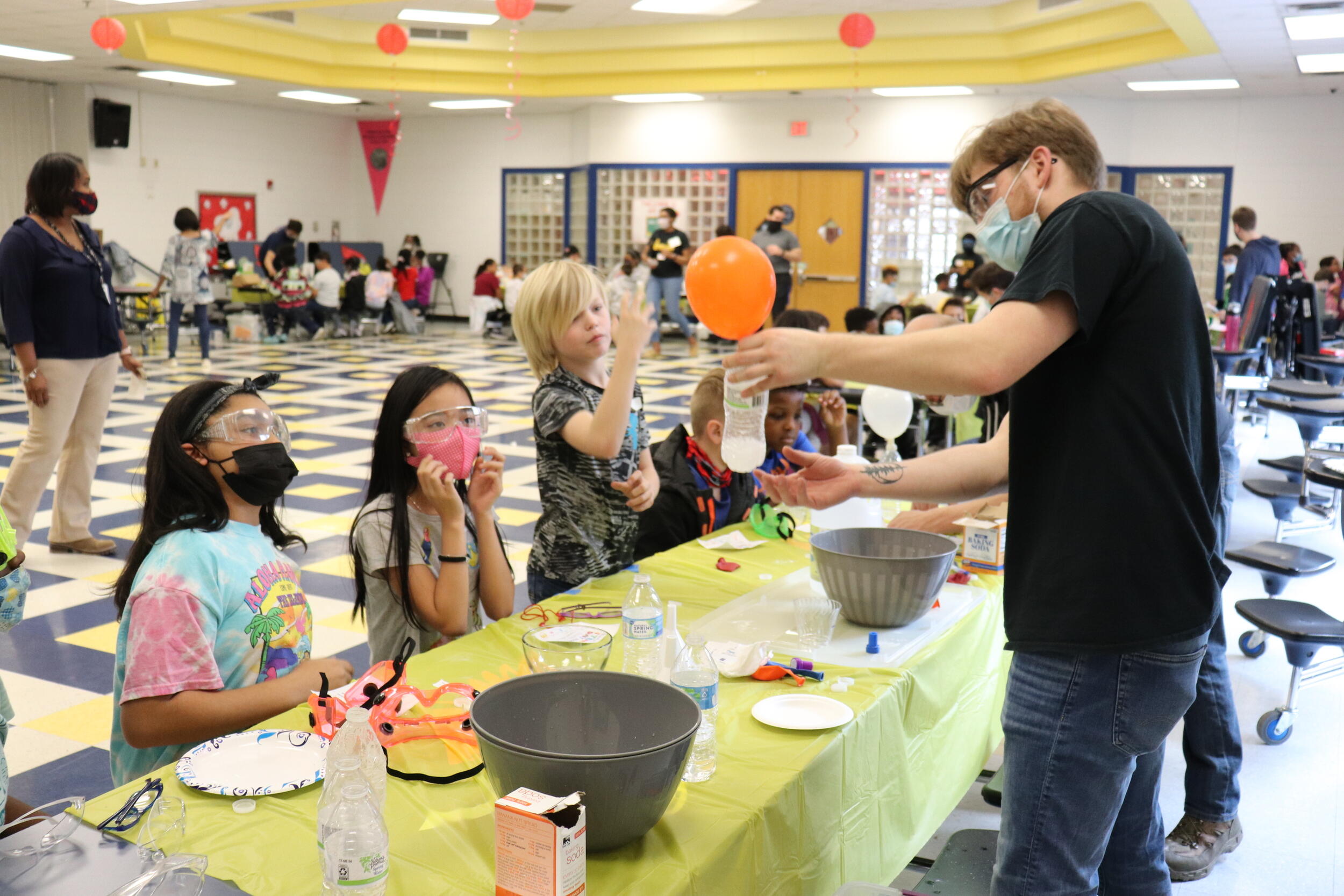 A VCU student showing students a balloon that was inflated with the chemical reaction of vinegar and baking soda in a bottle underneath it