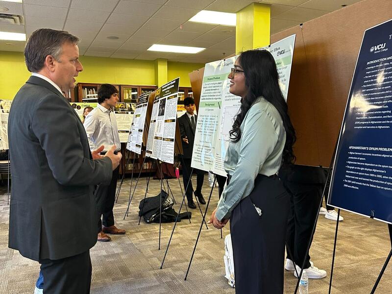 A photo of a woman standing in front of a research poster and speaking with a man. 