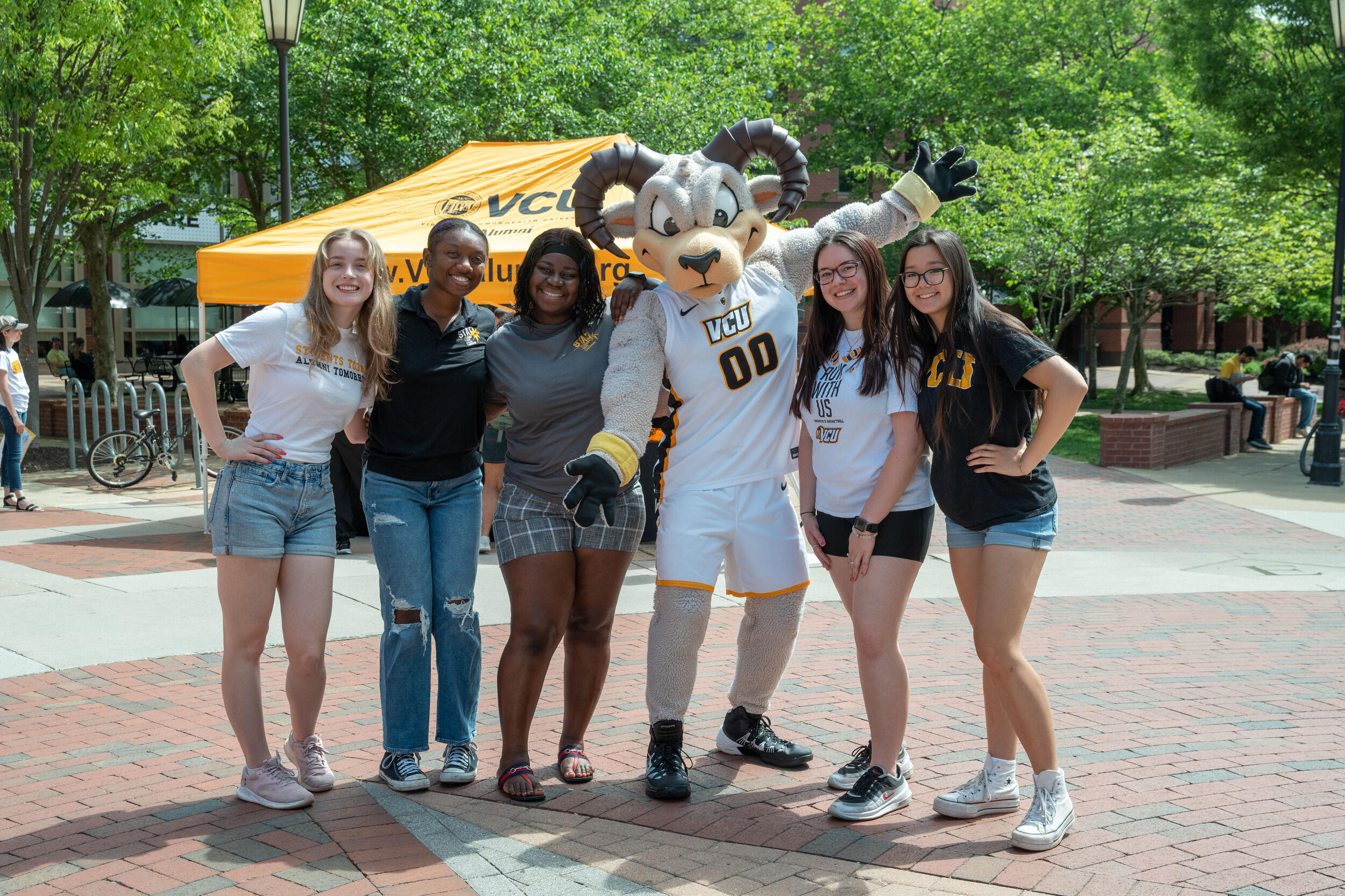 A photo of three people standing to the left of and two people standing to the right of Rodney the Ram. 
