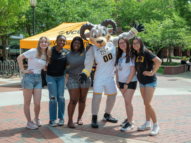 A photo of three people standing to the left of and two people standing to the right of Rodney the Ram. 