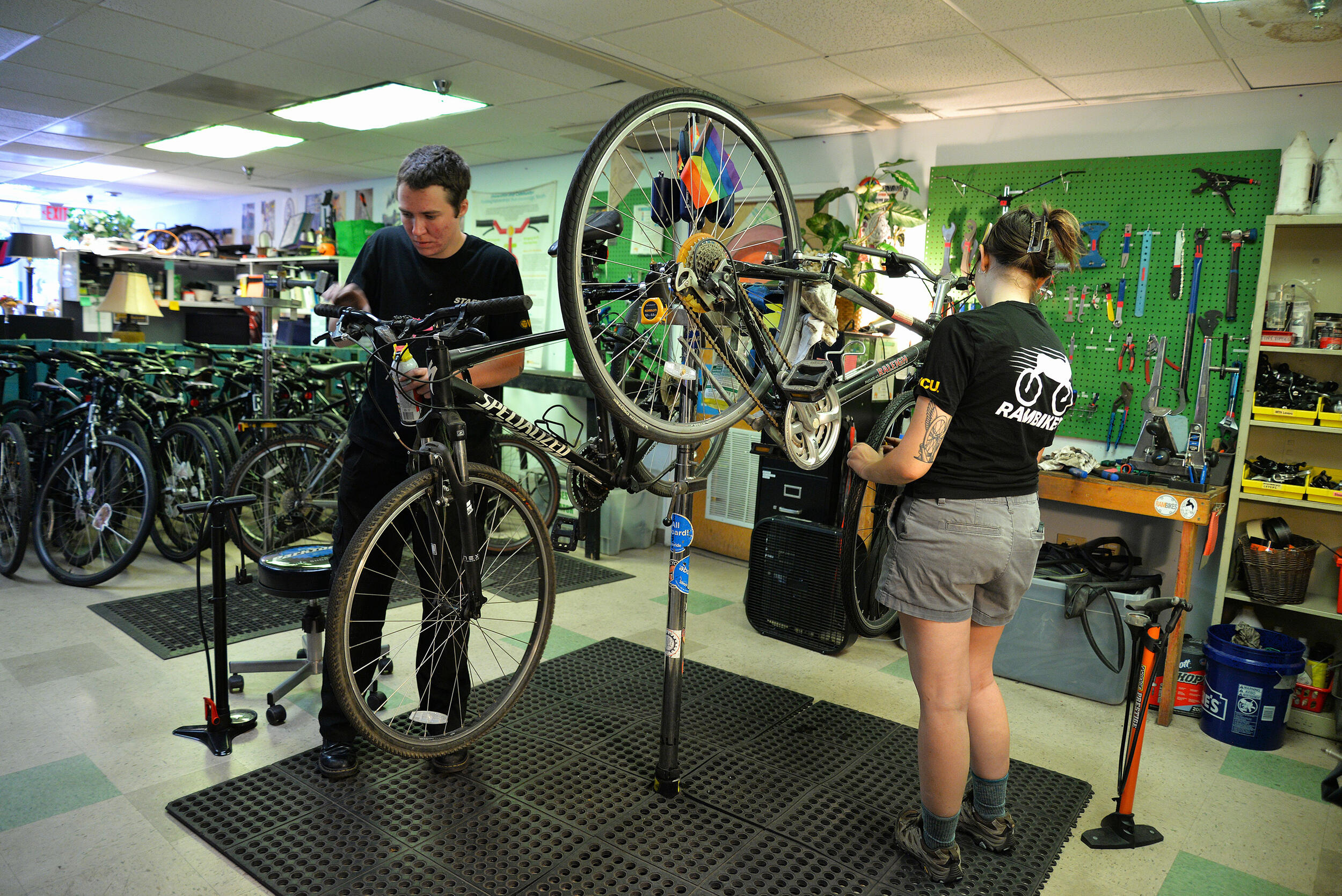 A photo of two people fixing two different bikes in a workshop. 