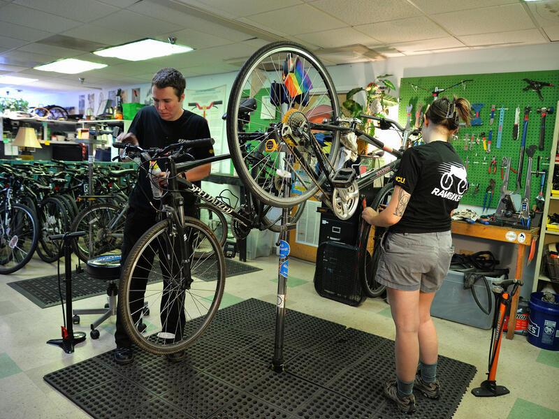 A photo of two people fixing two different bikes in a workshop. 