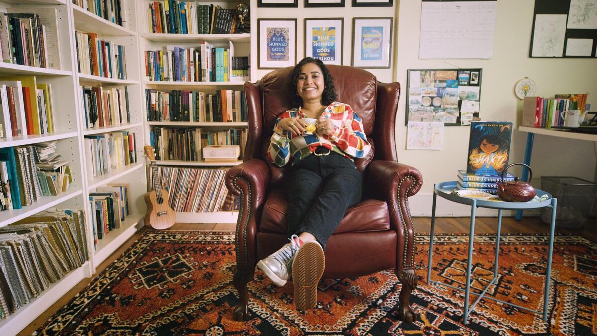 A photo of a woman sitting in a chair next to bookshelves filled with books. 