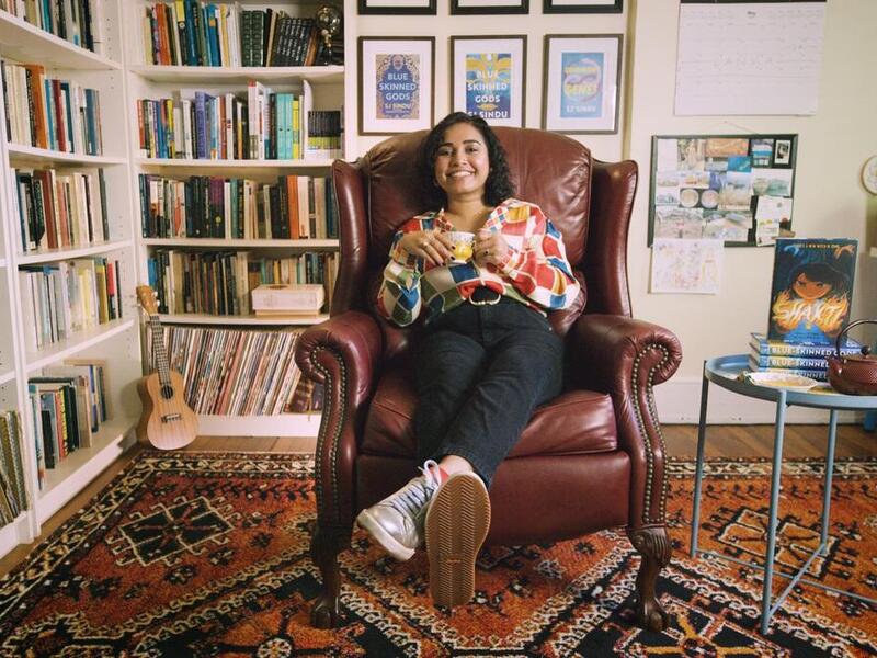 A photo of a woman sitting in a chair next to bookshelves filled with books. 