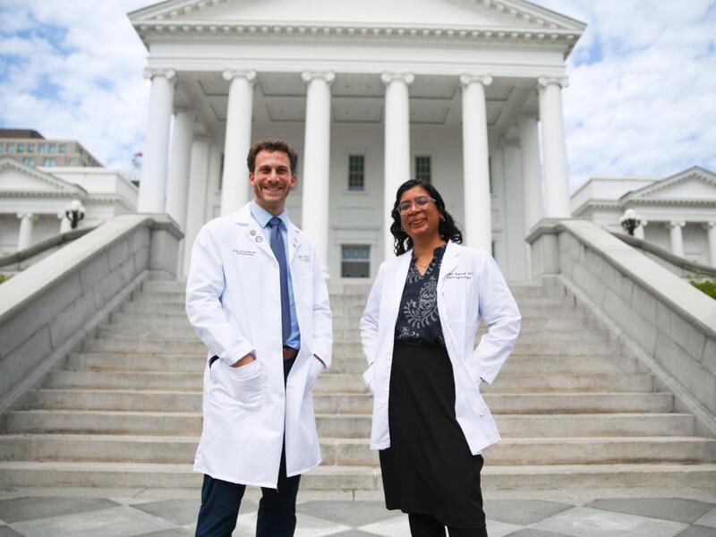 A photo of two people in doctor's coats standing on the steps of the Virginia State Capitol. 