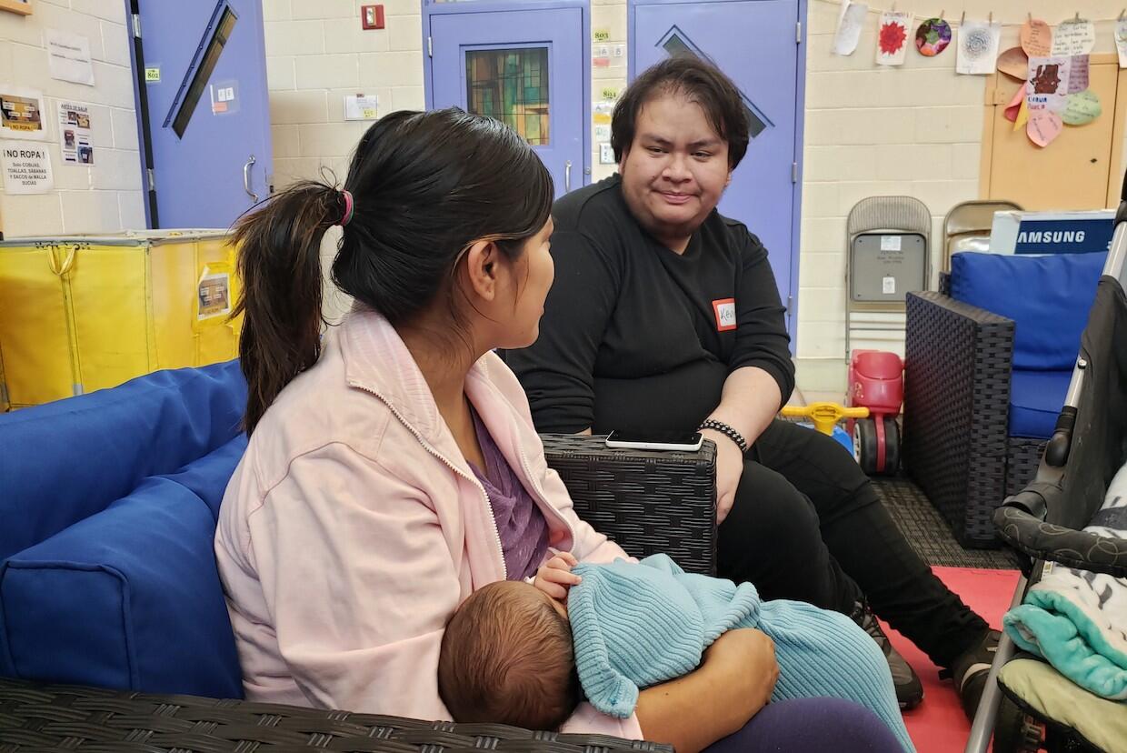 VCU student Kevin Armas Rodas in conversation with a young mother holding a baby.