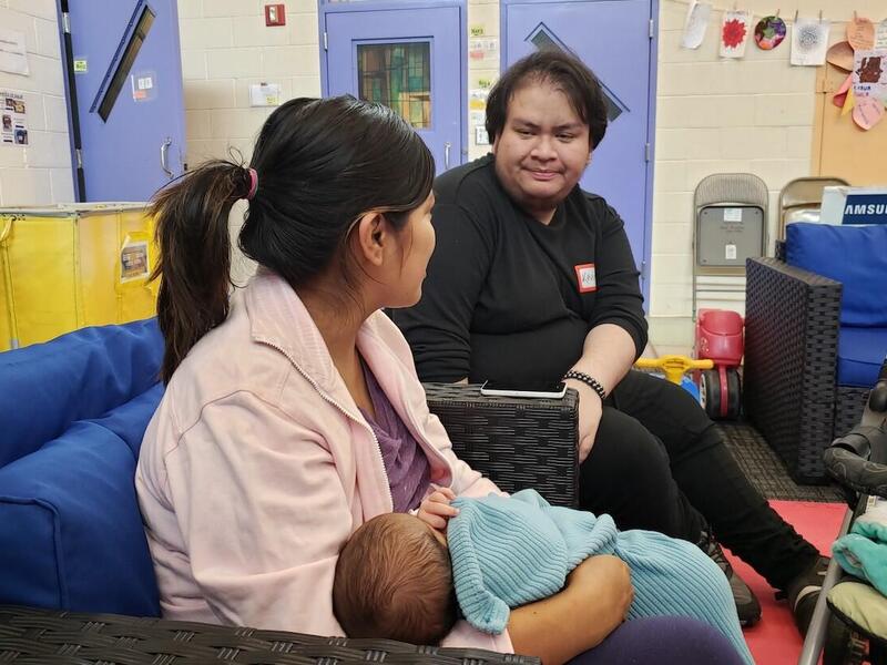 VCU student Kevin Armas Rodas in conversation with a young mother holding a baby.