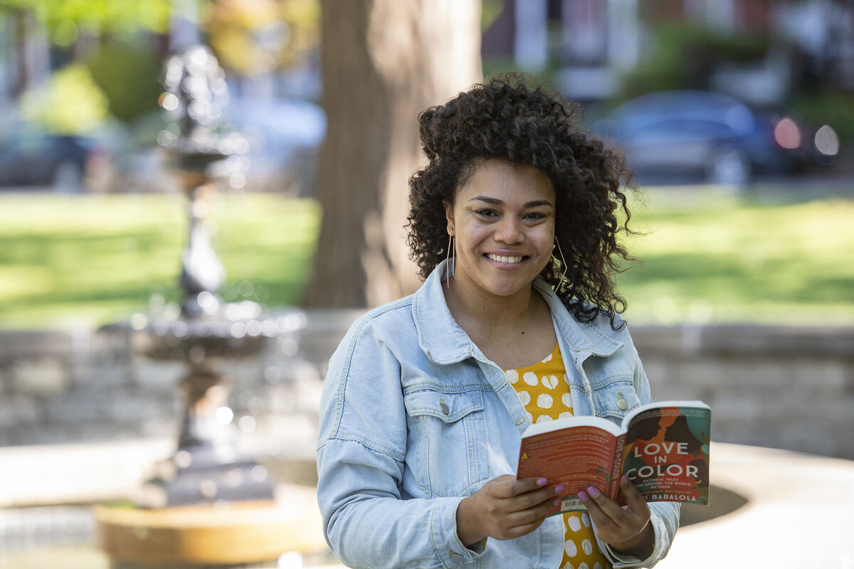 A woman standing outside in front of a fountain holding a book. 
