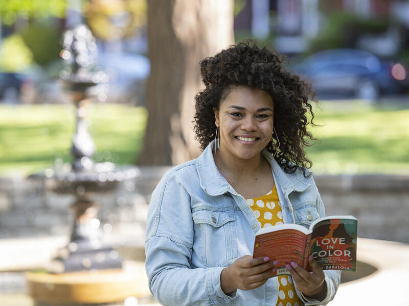 A woman standing outside in front of a fountain holding a book. 