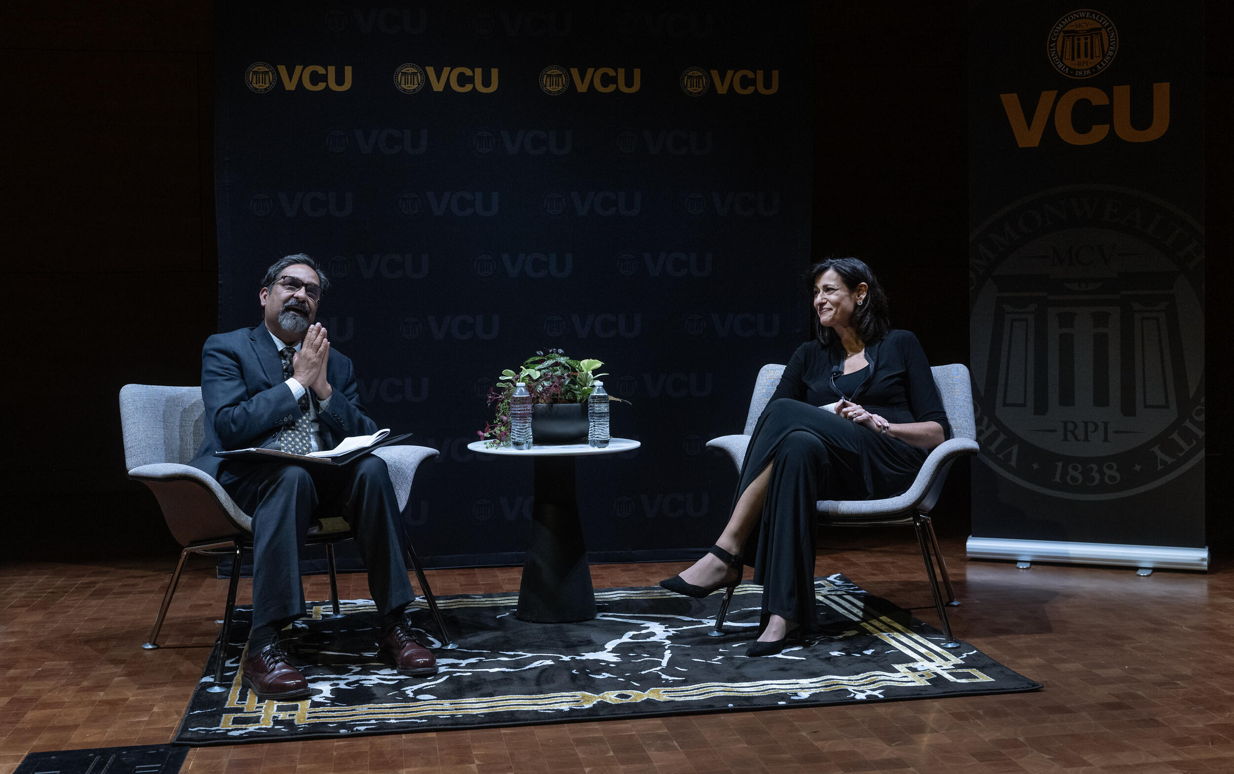 A photo of a man and a woman sitting in chairs on a stage. 