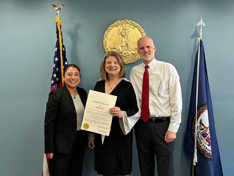 A photo fo three people standing. The person in the middle is holding a certificate. 