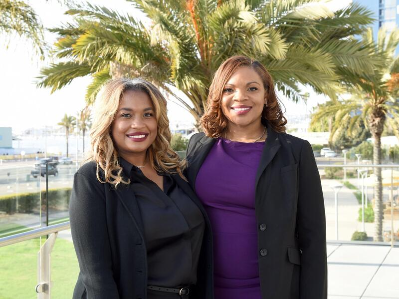 Two women standing next to each other in front of palm trees