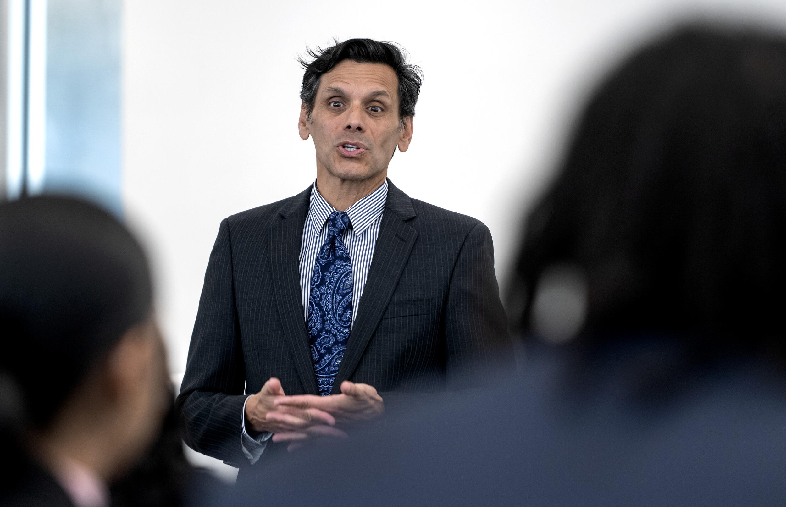 A photo of a man speaking in front of two blurred out people 