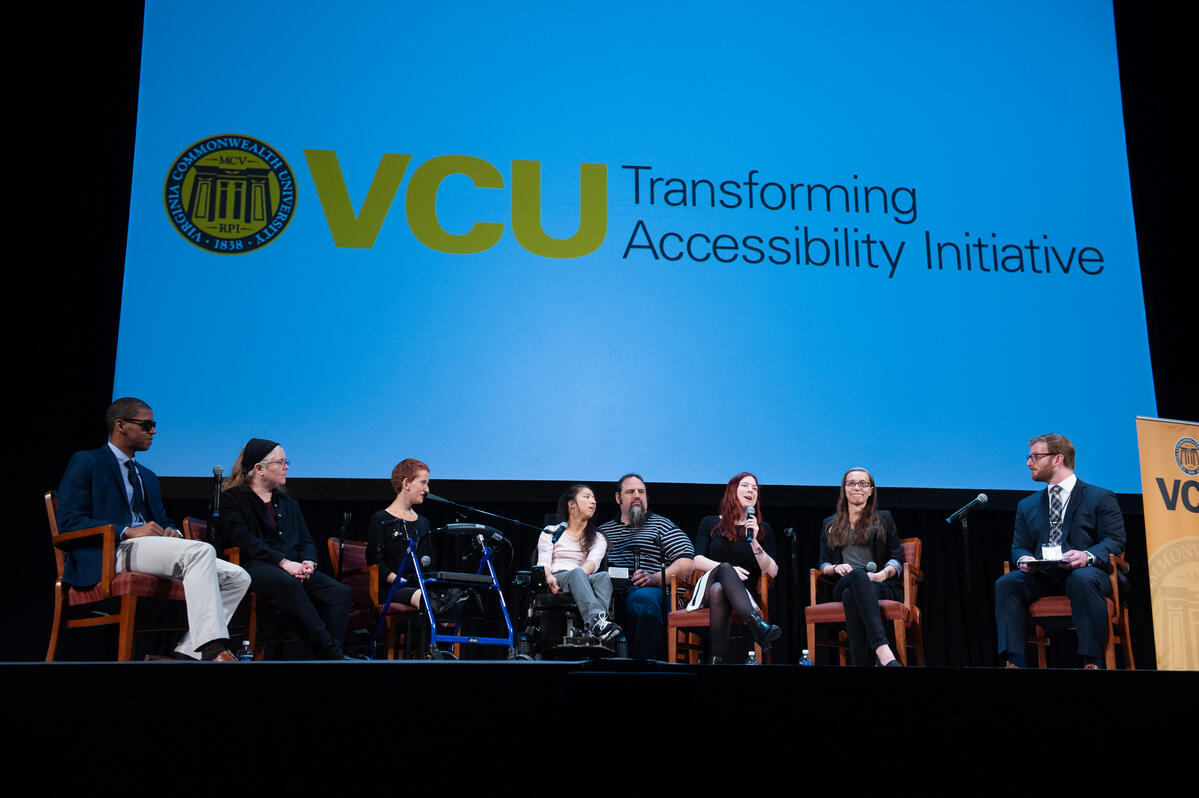 Eight people seated on a stage for a panel discussion. "Transforming Accessibility Initiative" and the V C U logo are displayed on the screen behind the panel participants.
