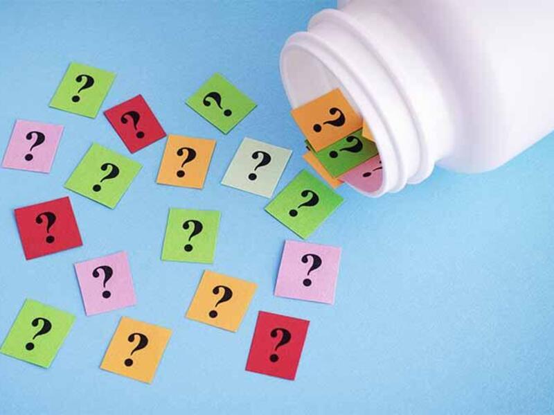 A pill bottle with different colored pieces of paper that have a question mark written on them spilling out of it