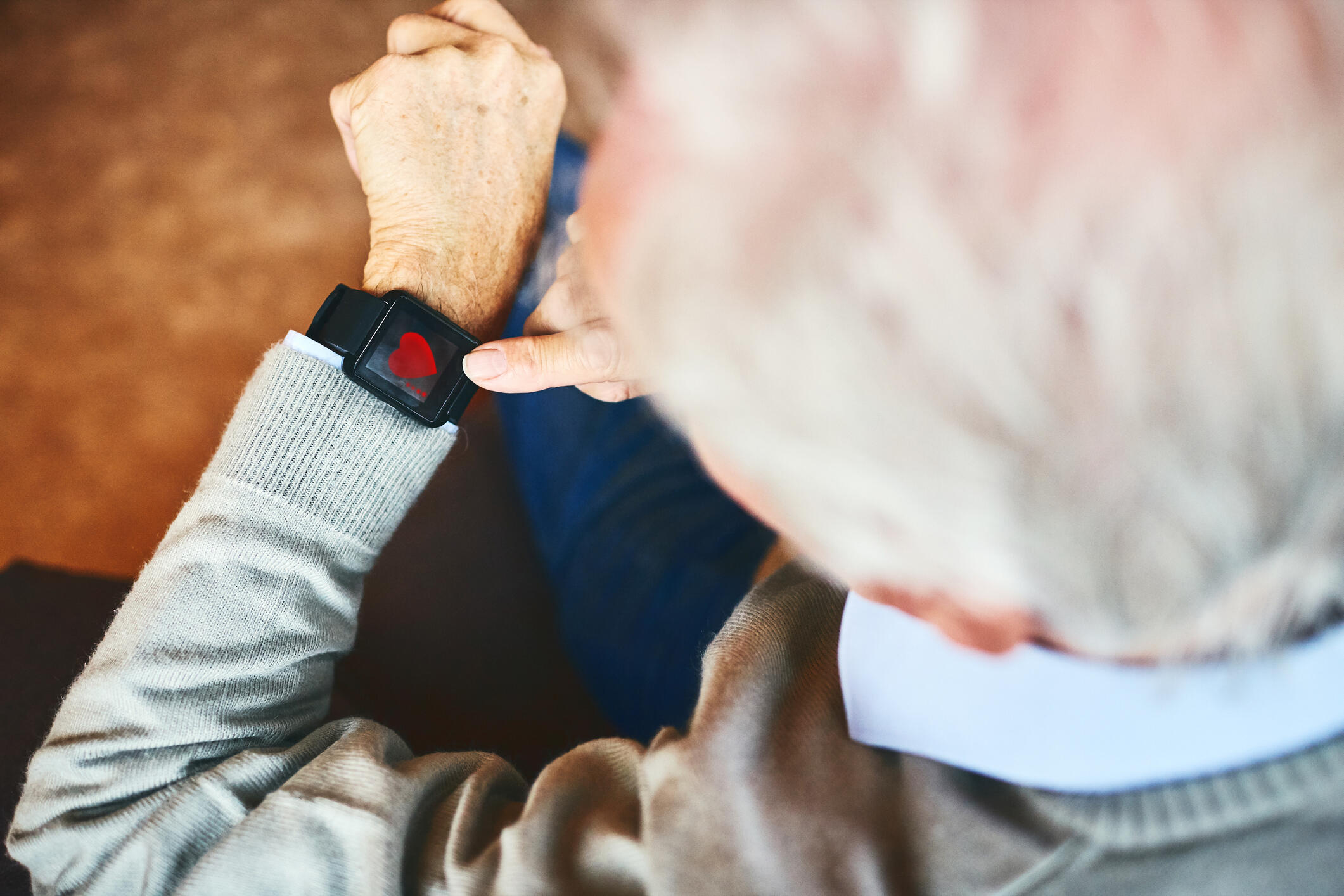 A photo of an old man looking down at a smart watch on his wrist. 