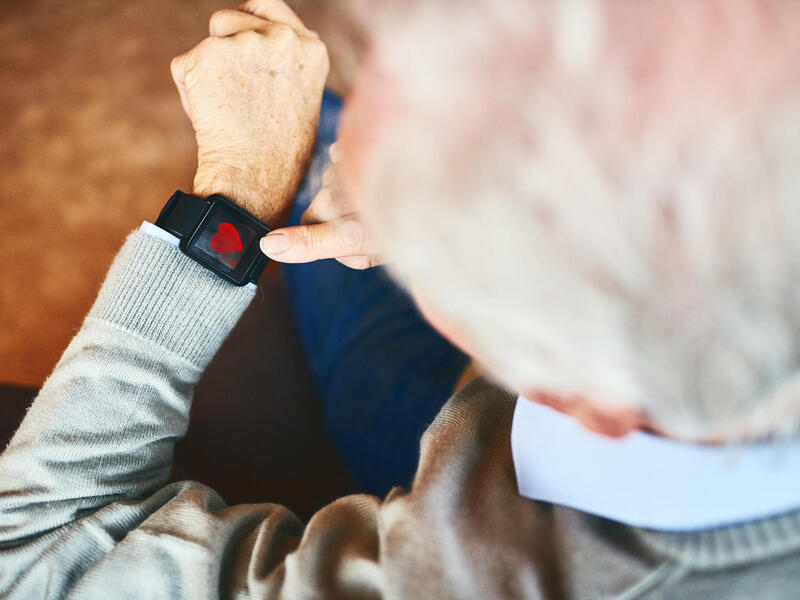 A photo of an old man looking down at a smart watch on his wrist. 