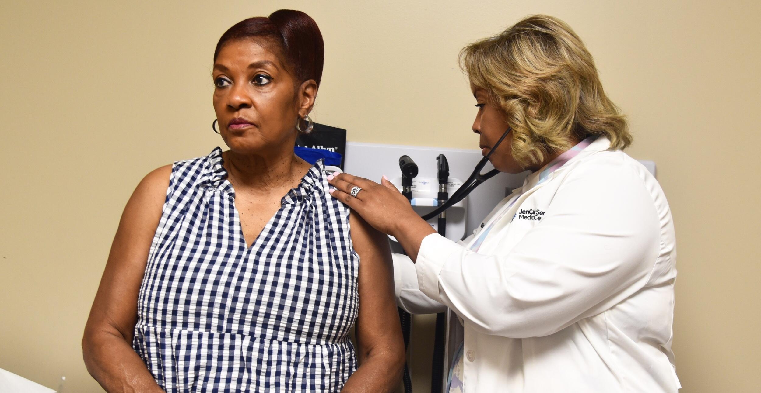 A woman sitting on an exam table while a doctor examines her. 