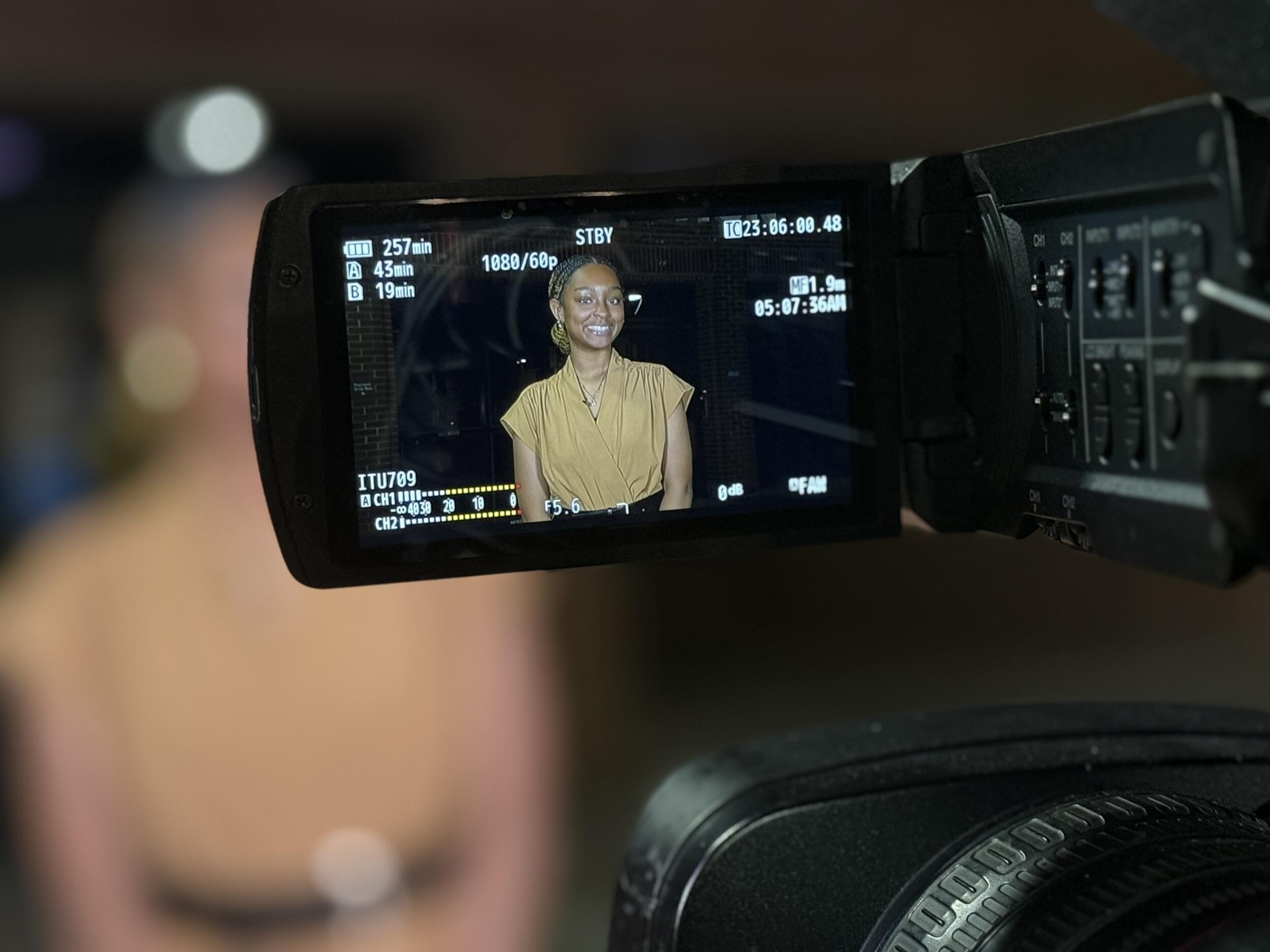 A photo of a screen of a video camera that is filming a woman. 
