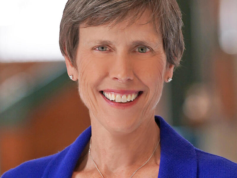 Jean Giddens smiling and wearing a blue blazer and a black blouse