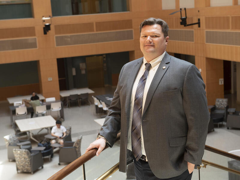 A man wearing a suit and tie standing with his hand resting on a stair railing 