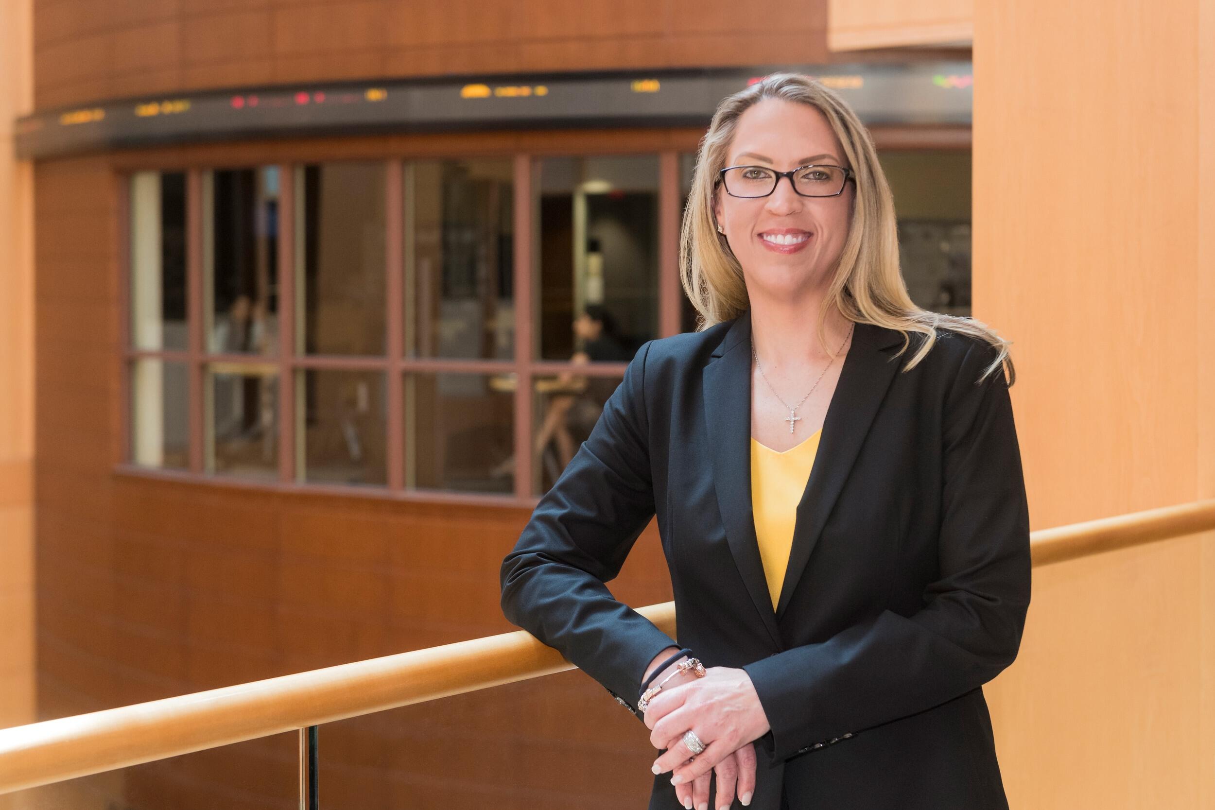 A photo of a woman from the waist up. She is resting one arm on a railing and smiling. 