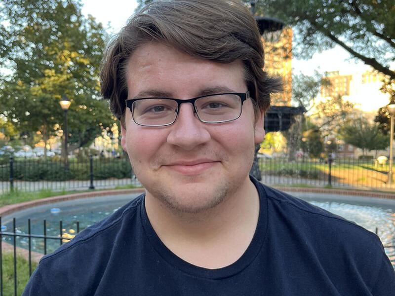 A photo of a man stadning in front of a fountain. 