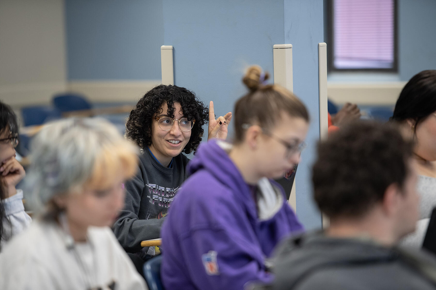 A photo of a woman raising her hand in the back of a classroom. 