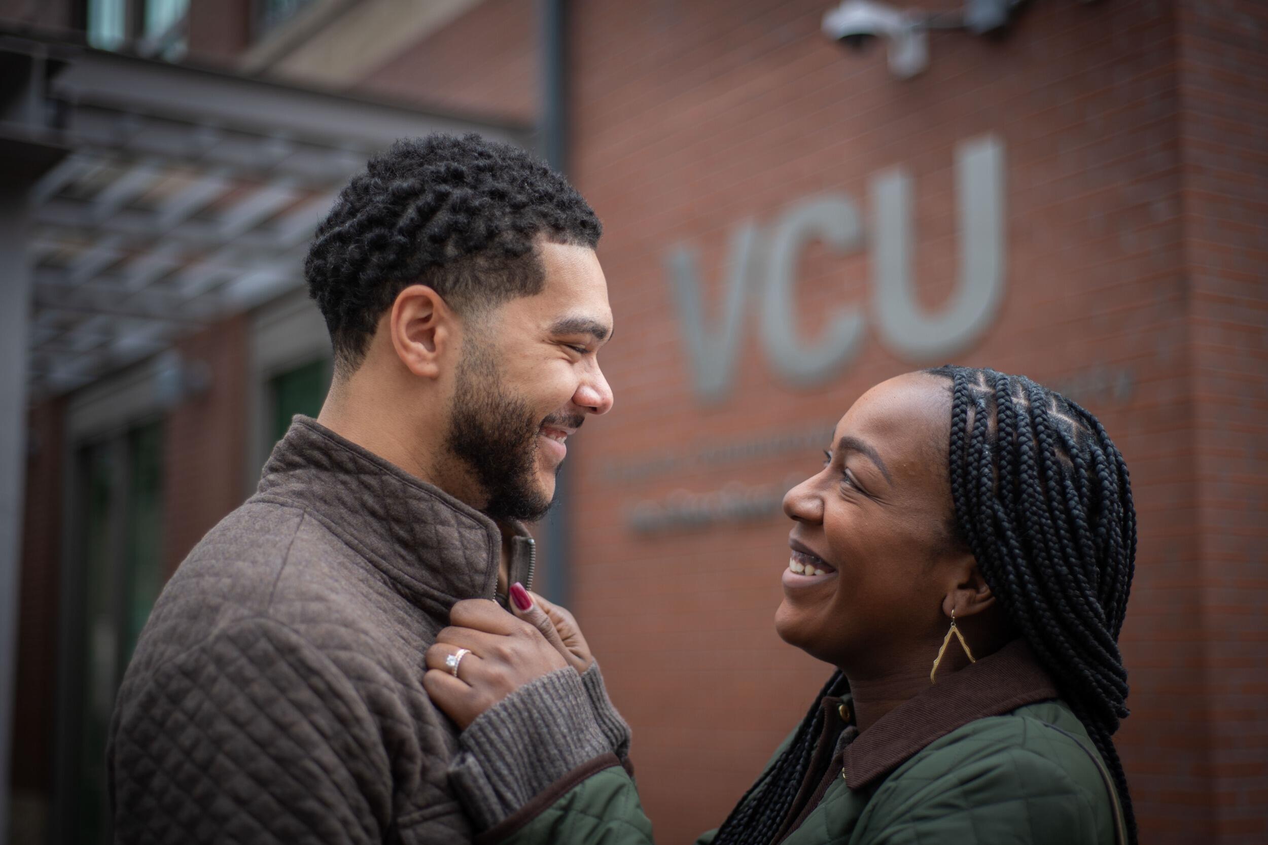 Ashawnna Godette holds Patrick Godette Jr.'s shirt collar as they smile and stare into each other's eyes, with a VCU sign on a building behind them.