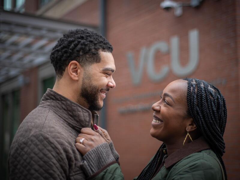 Ashawnna Godette holds Patrick Godette Jr.'s shirt collar as they smile and stare into each other's eyes, with a VCU sign on a building behind them.