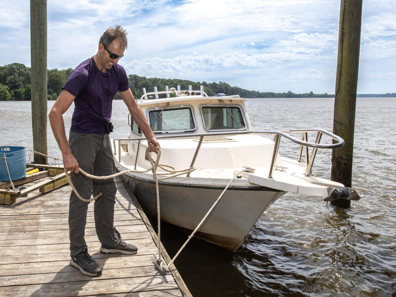 A photo on a boat dock holding onto a rope that is attached to a white boat. 