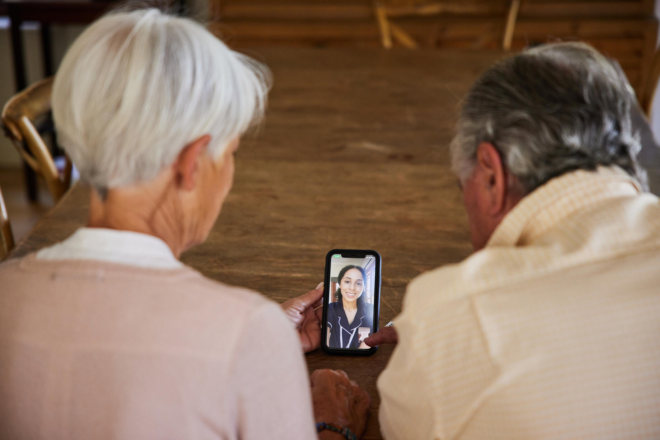 A photo of two elderly people holding a smart phone that has a video call with a medical care provider. 