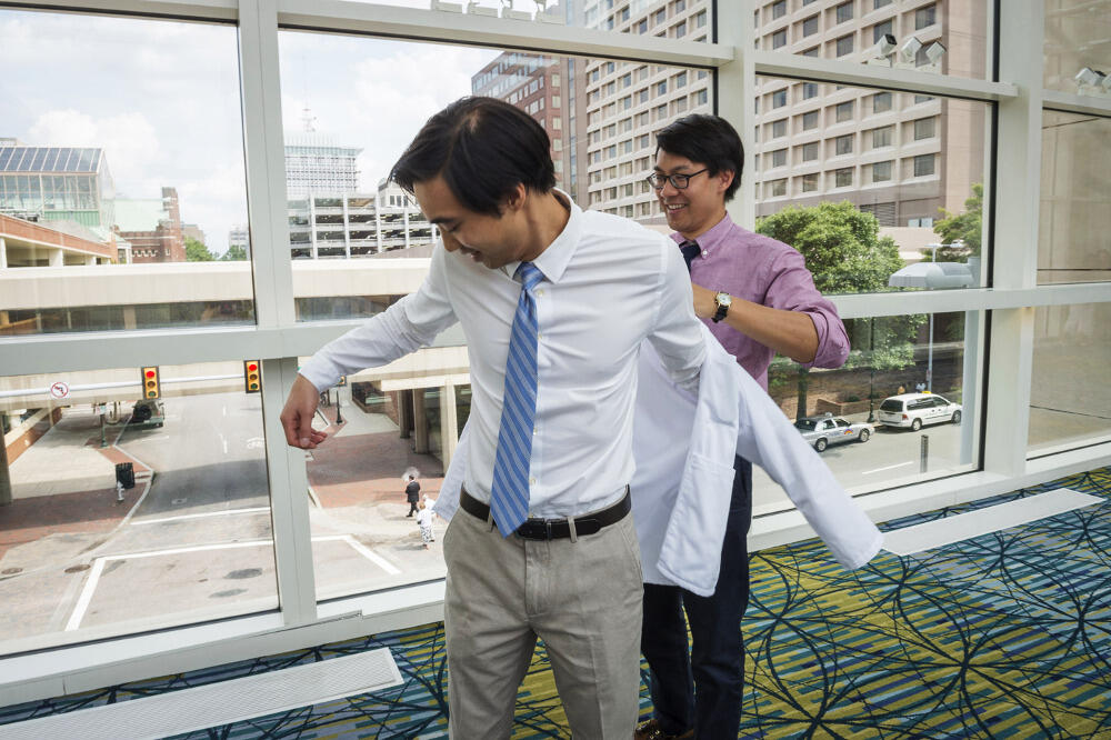 Eldest brother Brian Le helps his brother Christopher try on his new white coat. Photo by Allen Jones, VCU University Marketing.