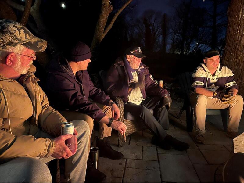 A photo of four men sitting outside in the dark in a semi-circle. 