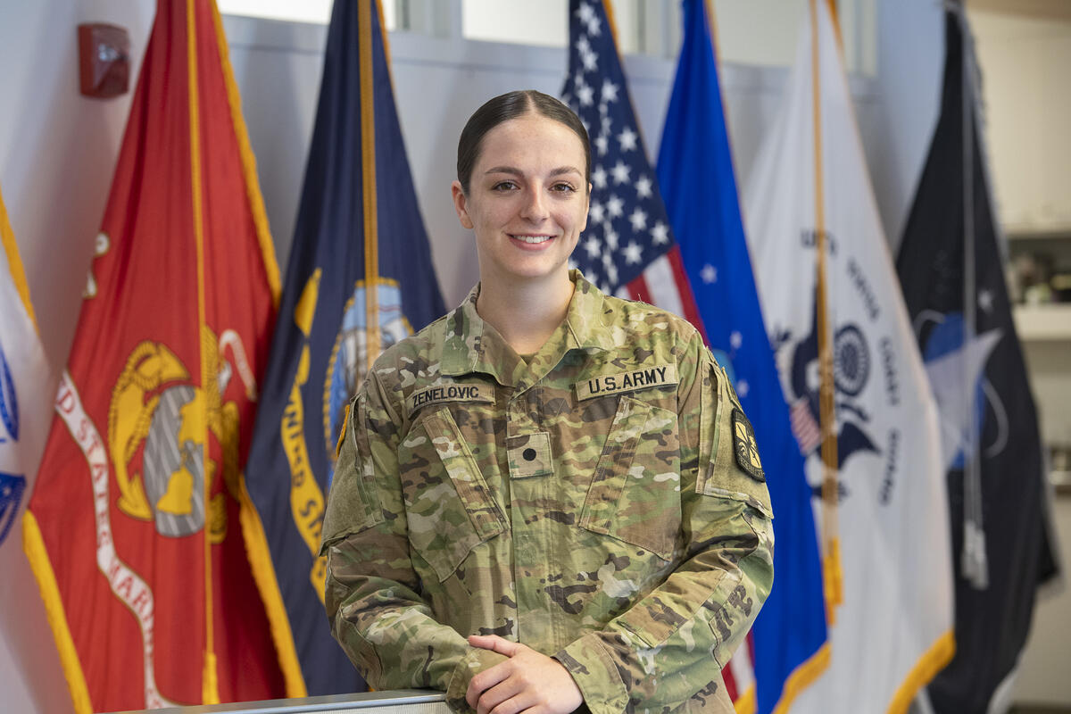 A woman wearing a U.S. Army uniform standing in front of flags. 