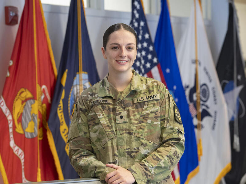 A woman wearing a U.S. Army uniform standing in front of flags. 
