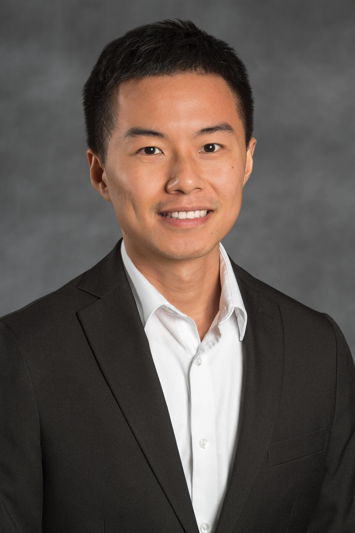 A photo of a man wering a black suit and white shirt from the chest up