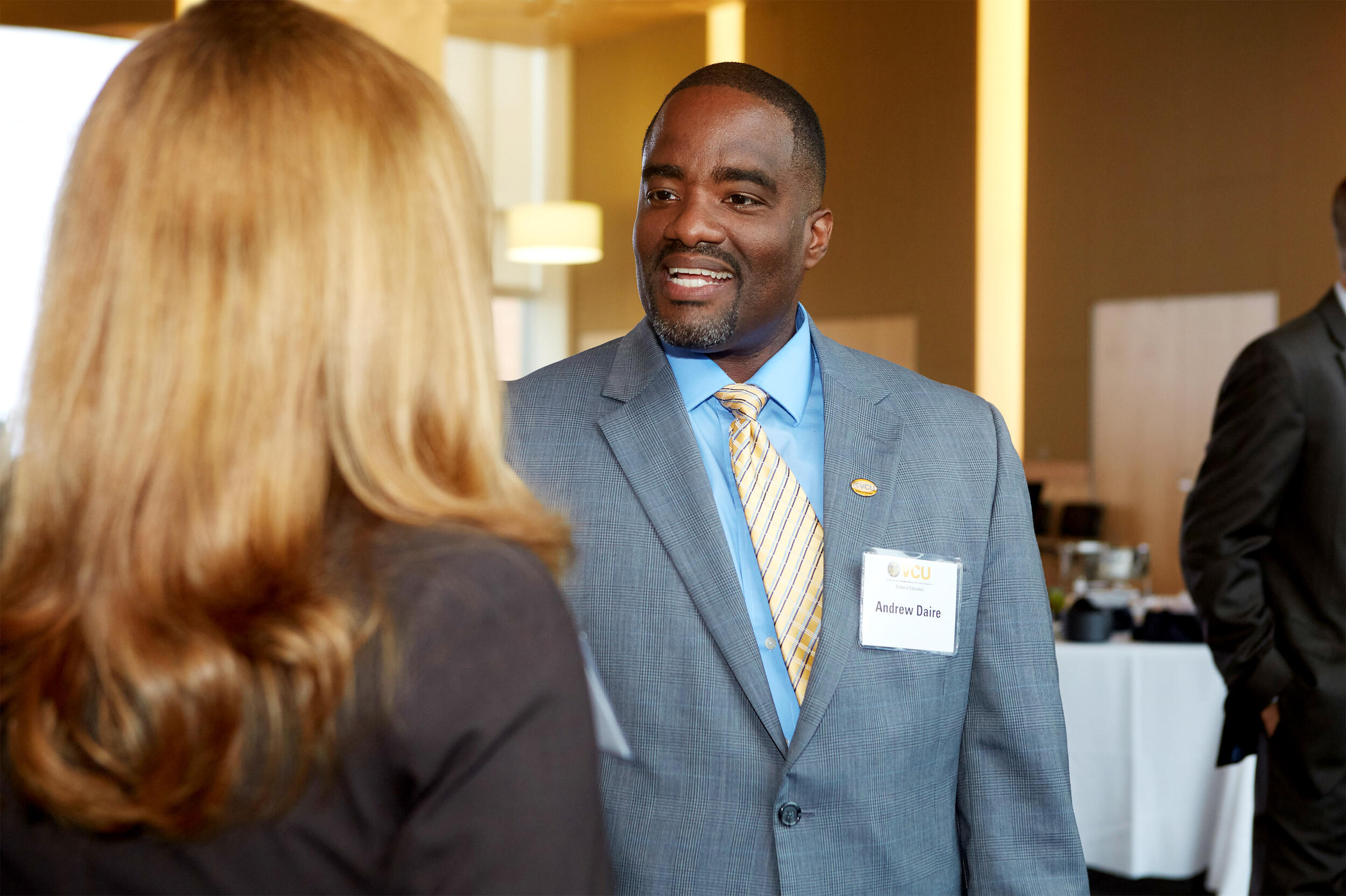 Andrew Daire smiling and talking to another individual.