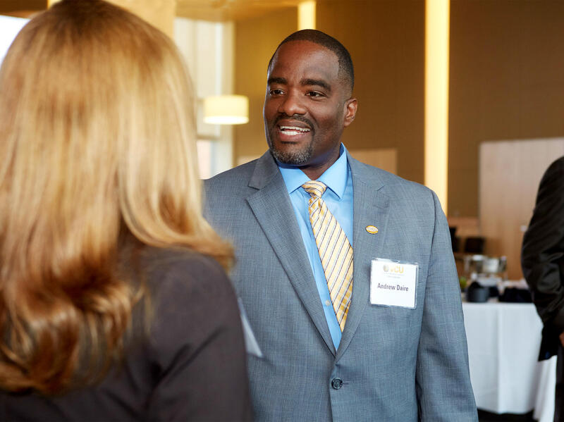 Andrew Daire smiling and talking to another individual.