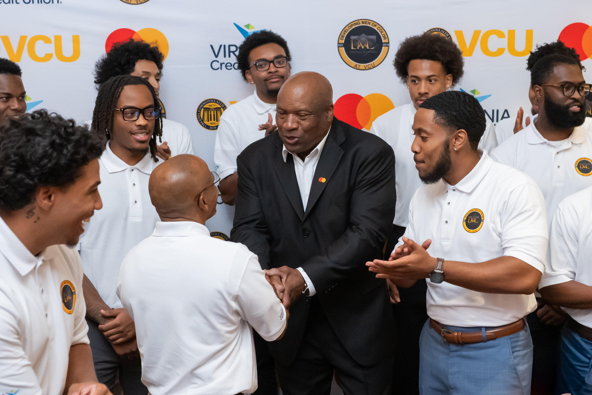 Bo Jackson, wearing a suit, shakes hands with a man in a white shirt and is surrounded by other men in white shirts.